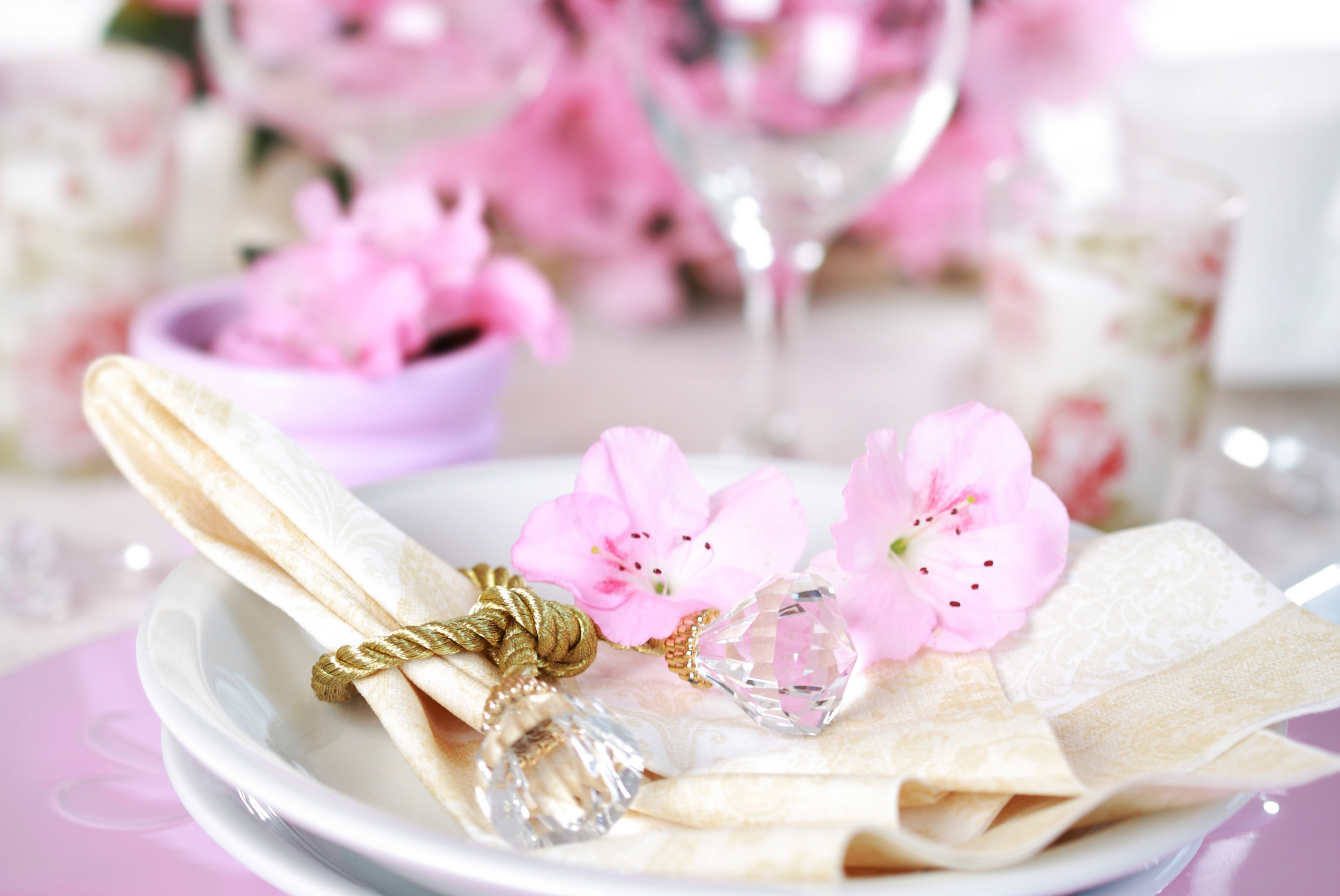 Teller, Serviette und goldfarbener Serviettenring mit rosa Blüten auf einer festlichen Tafel